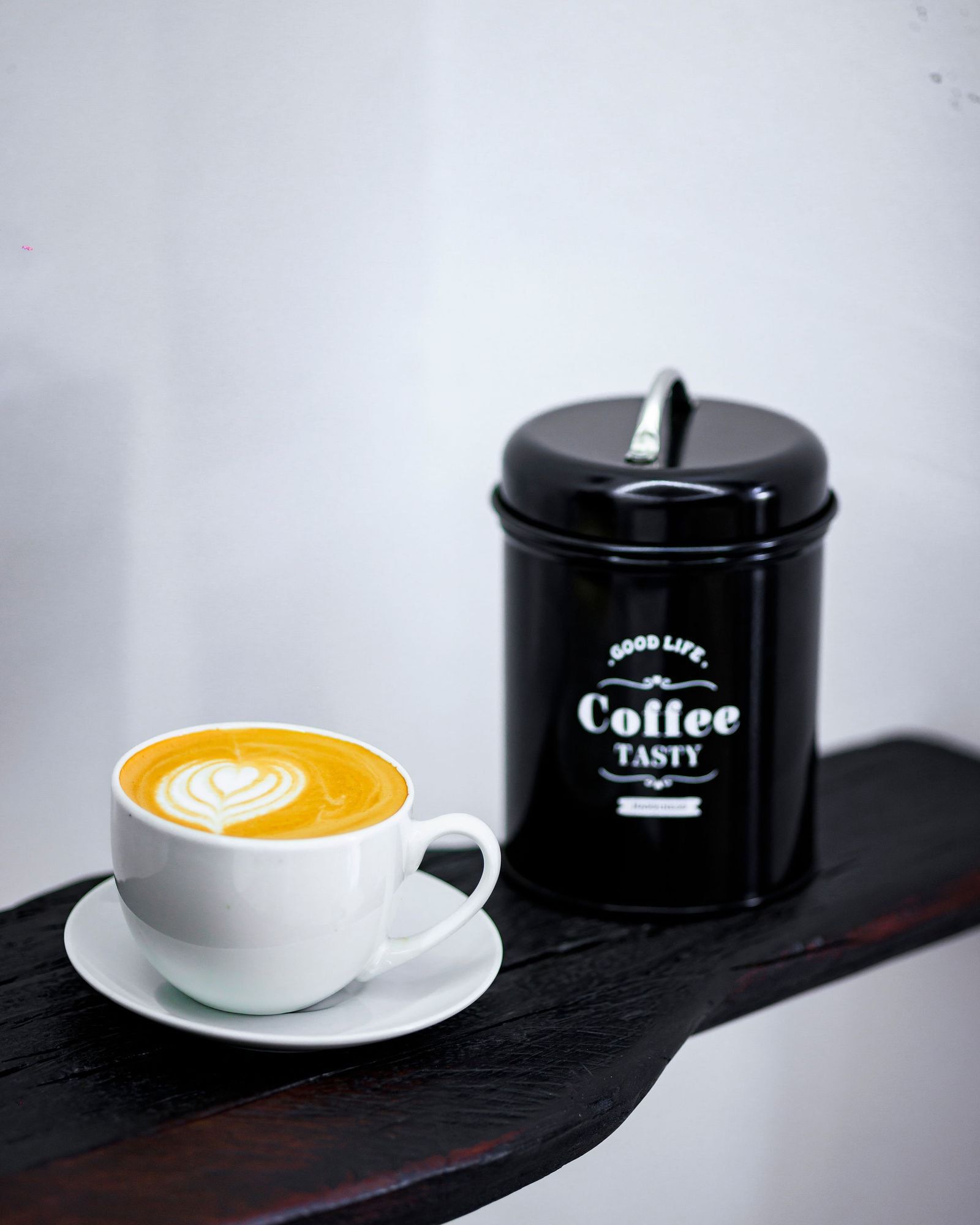 A cappuccino with latte art and a black coffee tin on the burnt wood shelf inside KTS Café