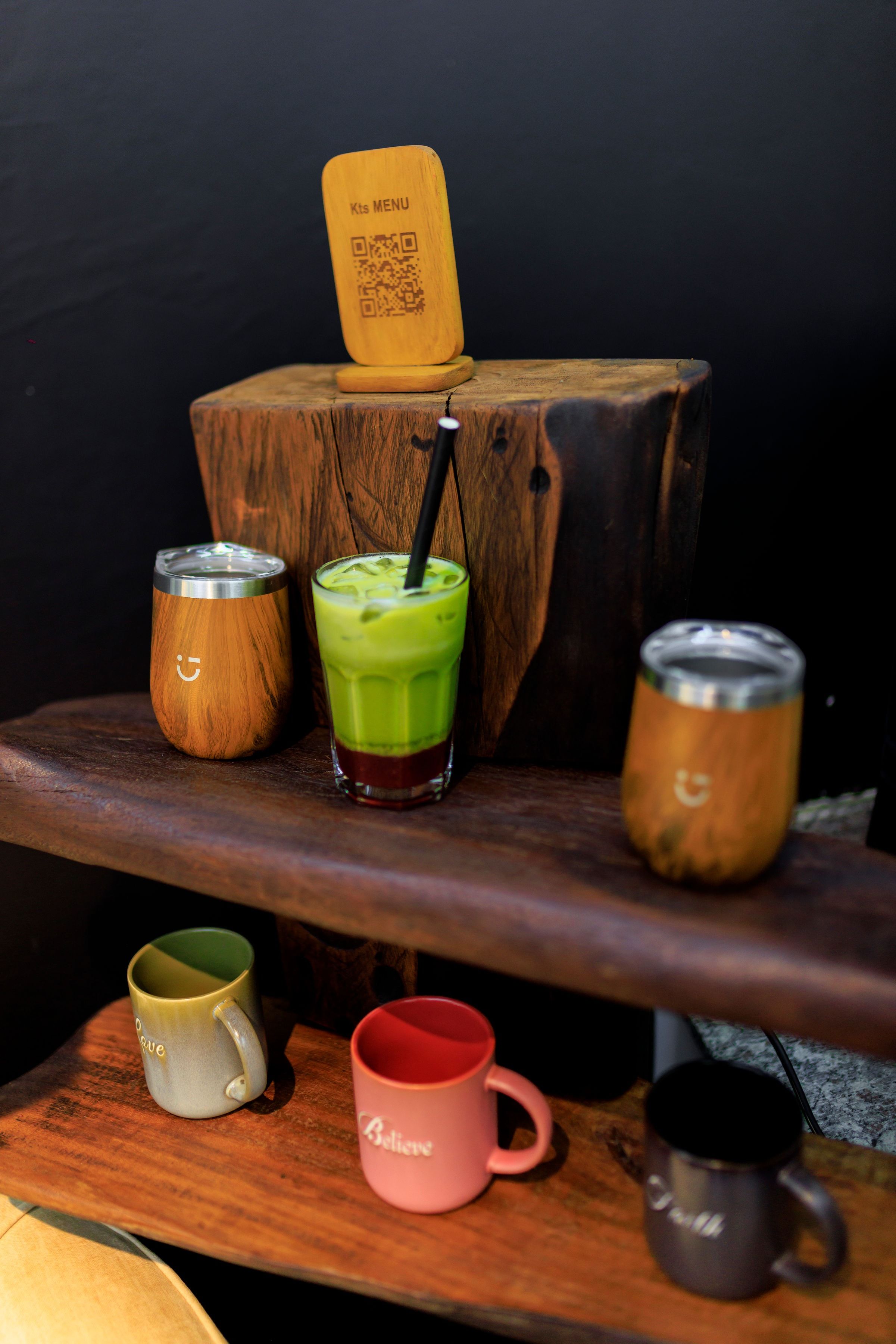 An iced matcha and KTS Café cups arranged on rustic wooden shelves