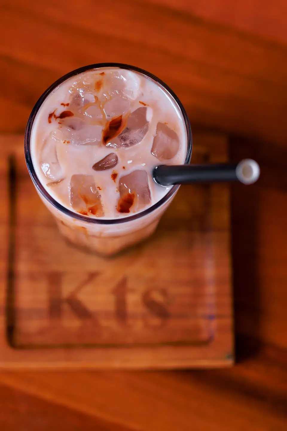 A top-down iced chocolate with syrup marbling on a branded KTS wooden board