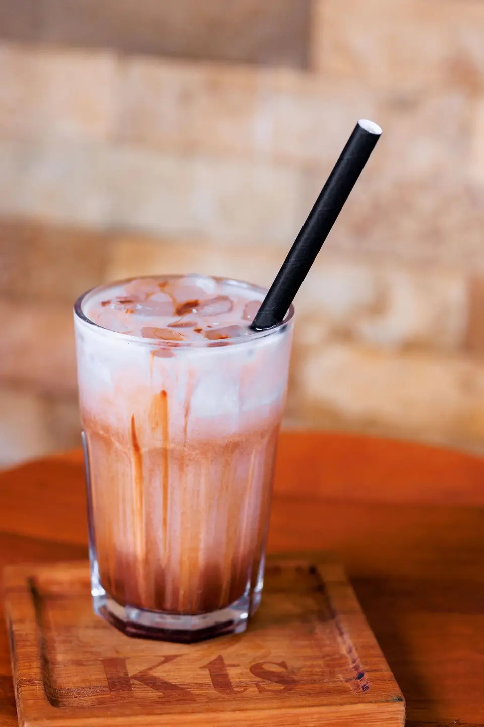 A creamy iced chocolate on a branded KTS serving board against the warm brick wall
