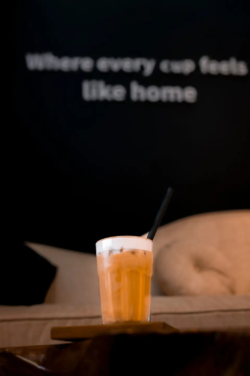 A foam-topped iced coffee on the lounge couch beneath the KTS Café wall lettering
