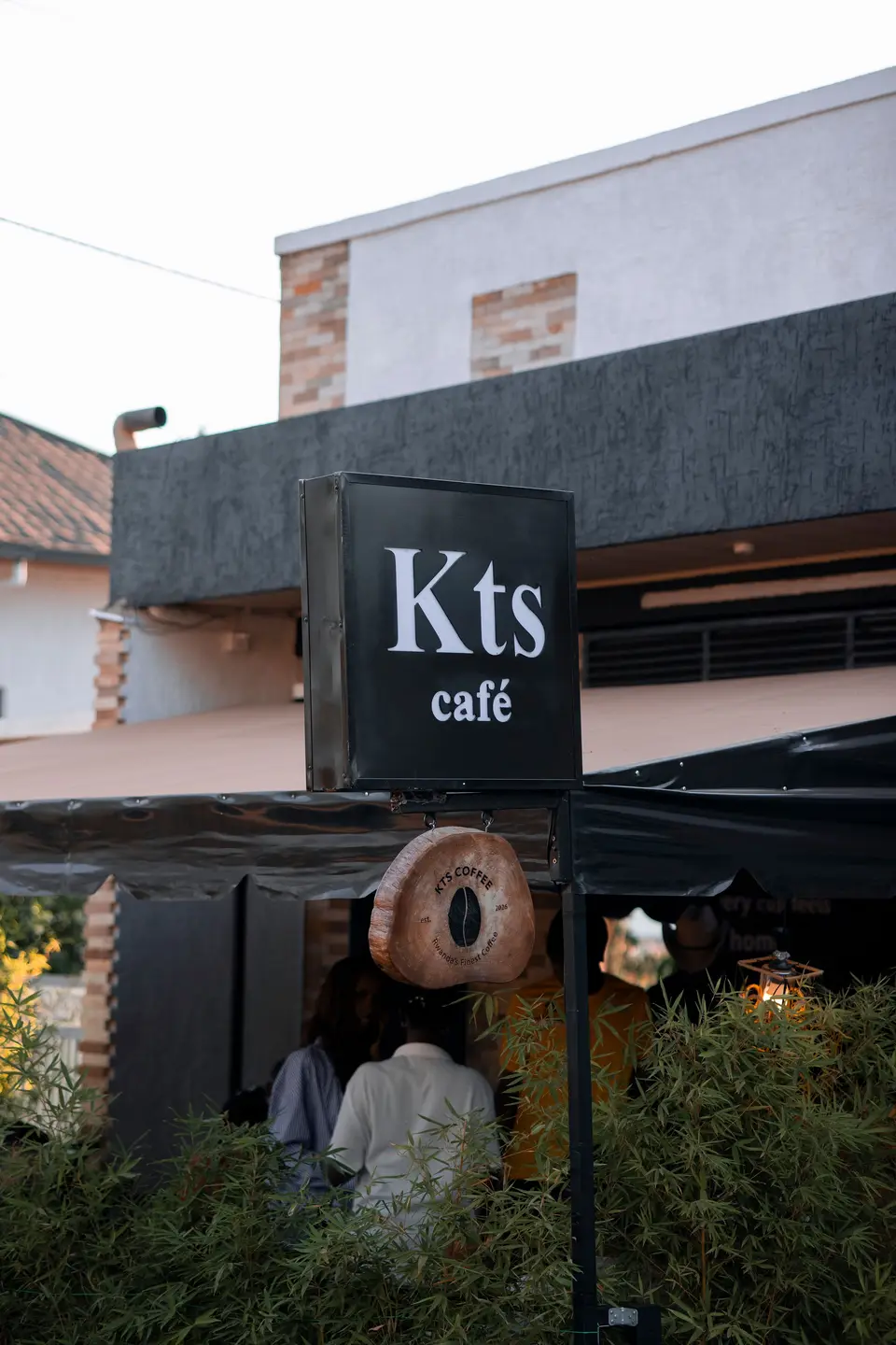 Guests gathered under the terrace awning behind the KTS Café street sign at dusk