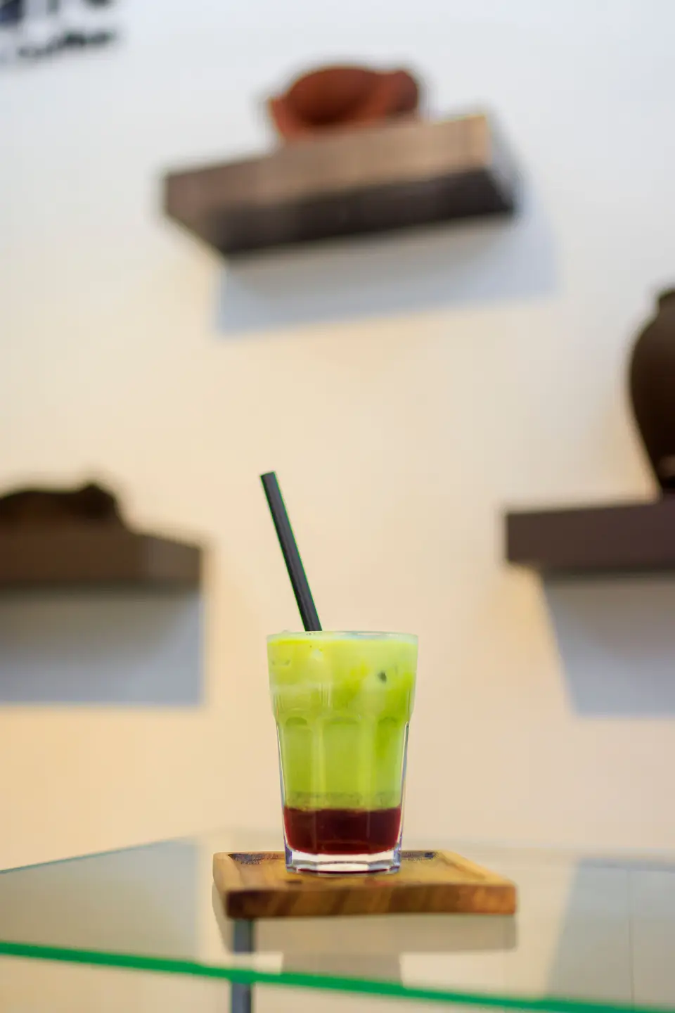 A vivid green matcha and berry cooler on a wooden coaster in front of the KTS Café pottery shelves
