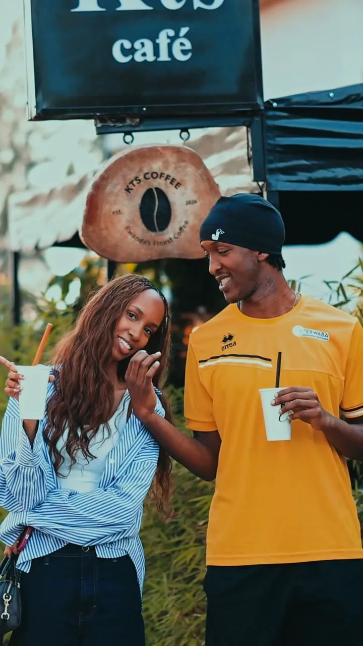 A couple holding KTS Café cups beneath the café sign and the KTS Coffee roundel